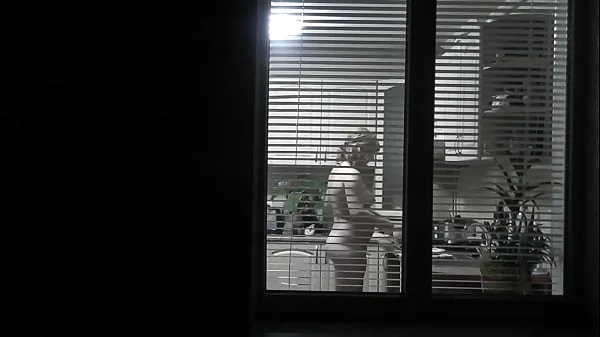 Peeping. Voyeur. Neighbor pervert voyeur in evening on street looks out window as naked sexy neighbor in kitchen prepares dinner for her husband. Naked in public. Naked at home. Family.  Outdoor